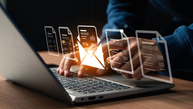 Hands typing on a laptop keyboard while digital invoice documents are displayed - Symbolizing the automation of e-invoicing processes